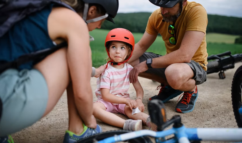 Child in a life jacket and helmet paddling a kayak with a parent on a calm lake